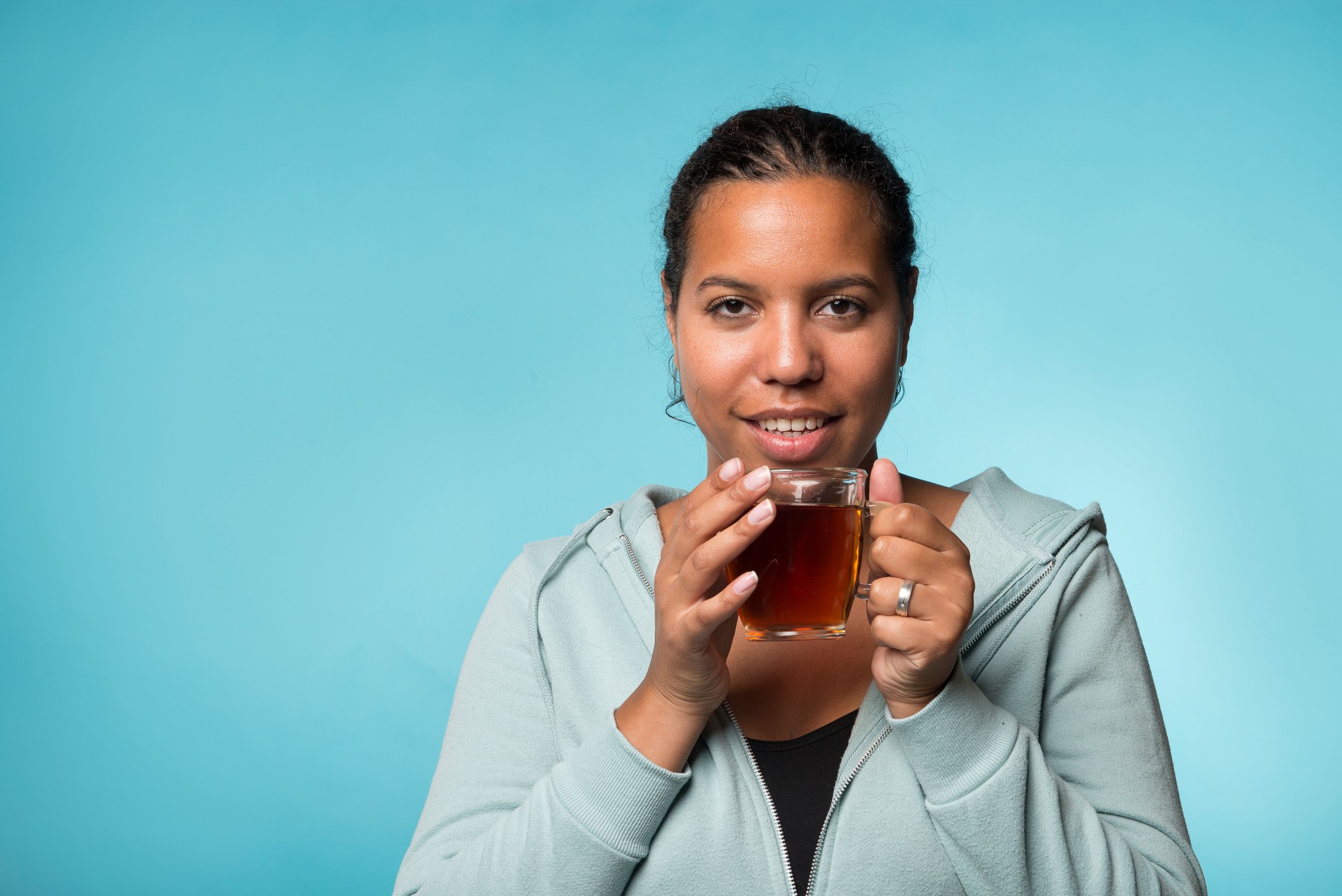 Beautiful young black woman drinking warm tea on a blue background