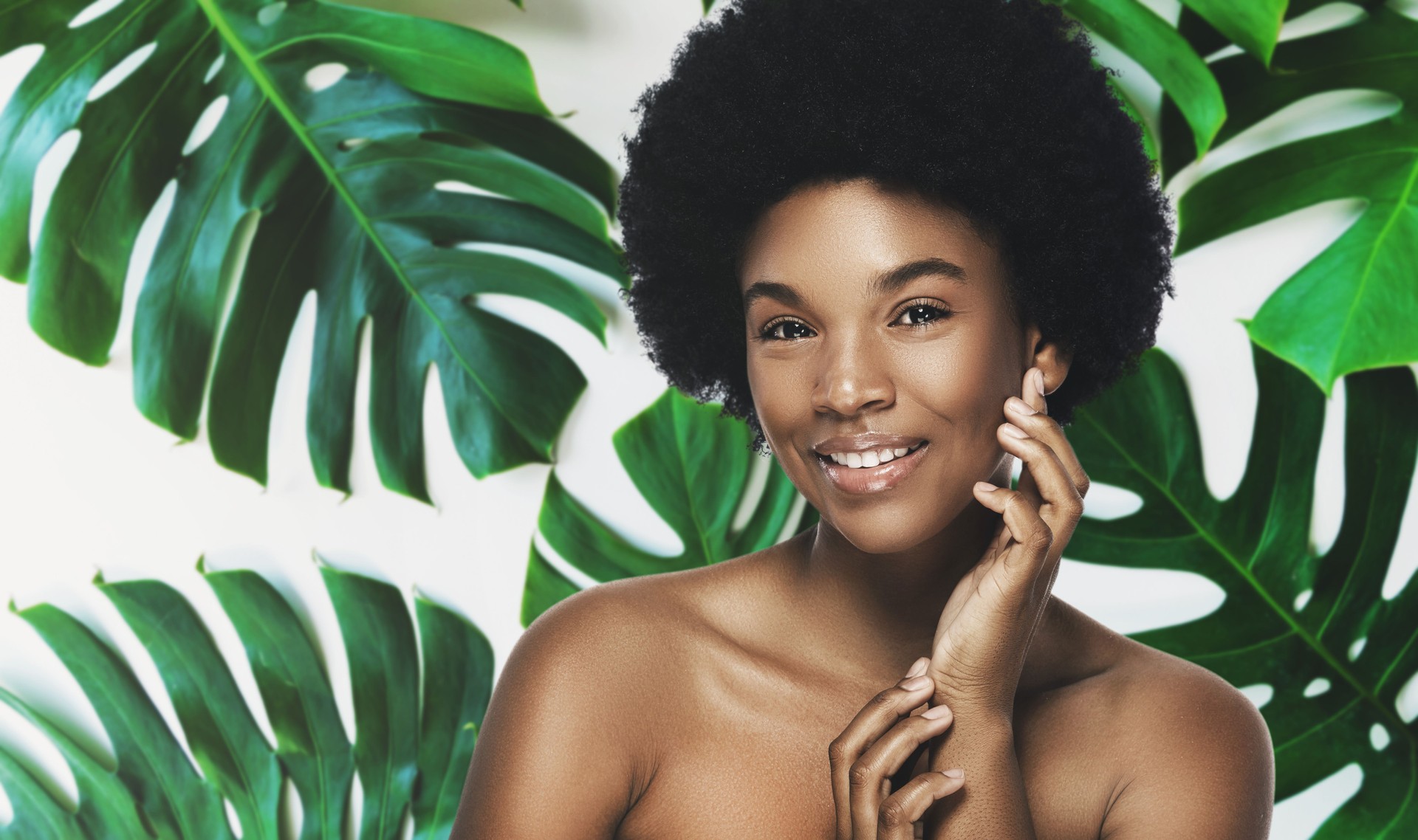 Young and beautiful African woman with perfect smooth skin in tropical leaves